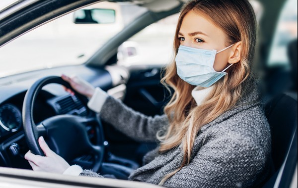 lady holding the steering wheel inside a car wearing a mask