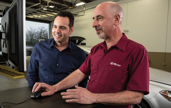 Jiffy Lube car dealer holding a mouse talking to a customer while showing the customer something in the monitor screen