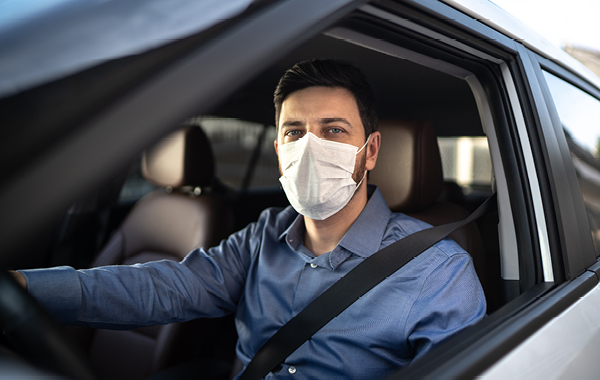 Jiffy Lube client wearing a mask sitting inside his car holding the steering wheel