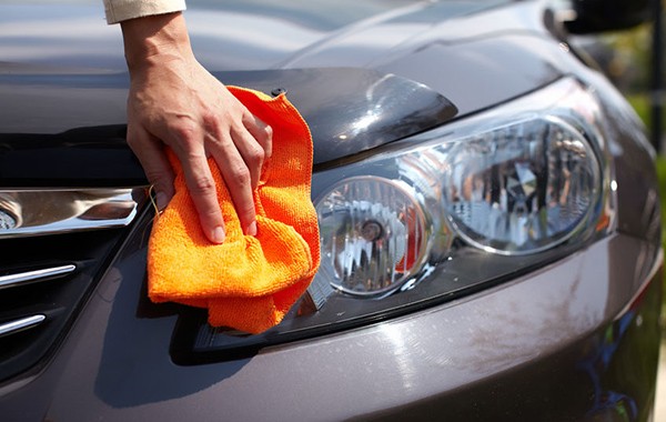 hand using an orange rug to clean a car's headlight