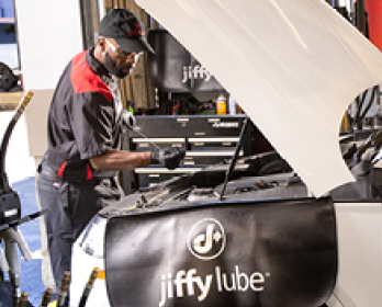 Jiffy Lube car expert checking the inside of a car's hood.